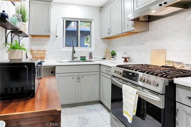 kitchen with range hood, decorative backsplash, gray cabinetry, sink, and stainless steel range with gas cooktop