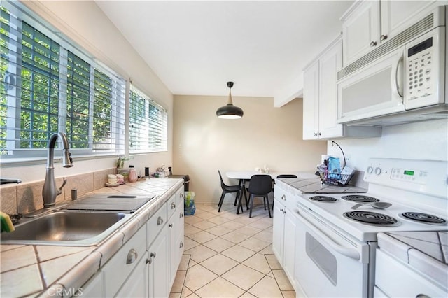 kitchen featuring white appliances, tile counters, hanging light fixtures, sink, and white cabinetry