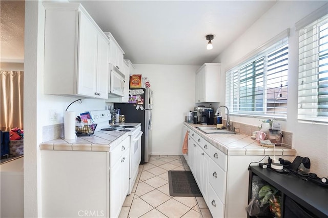 kitchen featuring white appliances, tile countertops, white cabinets, light tile patterned flooring, and sink