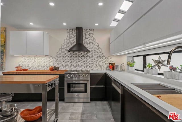 kitchen featuring dishwashing machine, white cabinets, high end range, wall chimney range hood, and sink