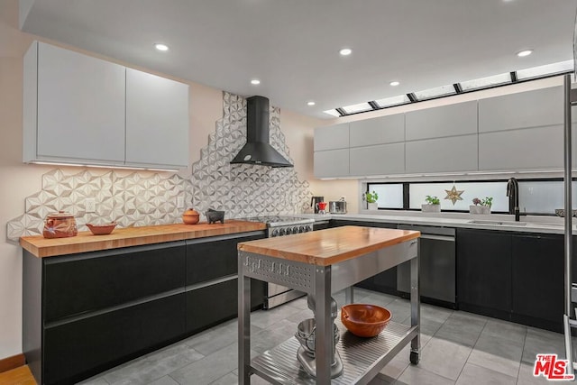 kitchen with butcher block countertops, sink, white cabinetry, stainless steel appliances, and wall chimney exhaust hood