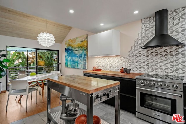 kitchen featuring decorative light fixtures, stainless steel stove, white cabinetry, wall chimney exhaust hood, and butcher block counters