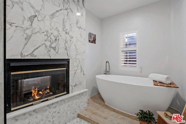 bathroom featuring a tub to relax in, wood-type flooring, and a fireplace