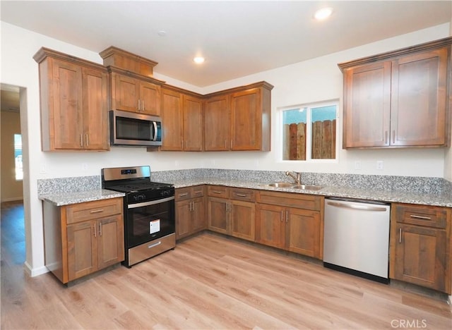 kitchen with stainless steel appliances, light stone countertops, sink, and light wood-type flooring