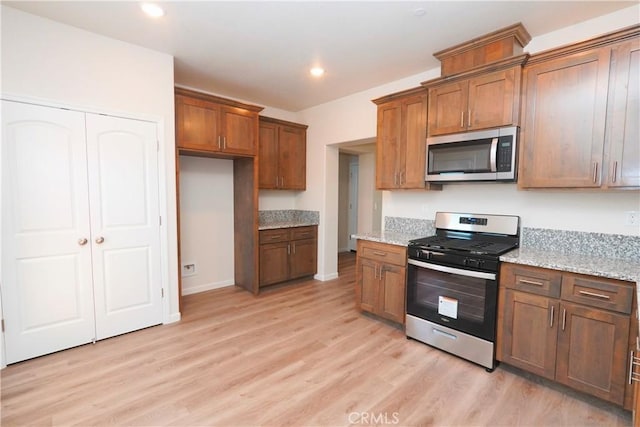 kitchen with stainless steel appliances, light stone countertops, and light hardwood / wood-style flooring