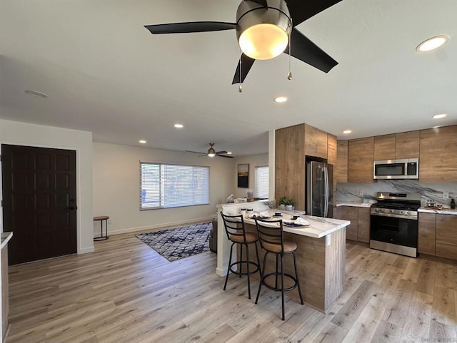 kitchen featuring a center island, light hardwood / wood-style floors, tasteful backsplash, a breakfast bar area, and appliances with stainless steel finishes