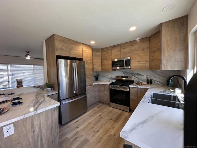 kitchen featuring stainless steel appliances, light wood-type flooring, ceiling fan, sink, and backsplash