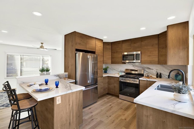 kitchen with appliances with stainless steel finishes, a kitchen bar, sink, kitchen peninsula, and light hardwood / wood-style flooring