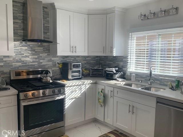 kitchen with appliances with stainless steel finishes, wall chimney exhaust hood, backsplash, and white cabinetry