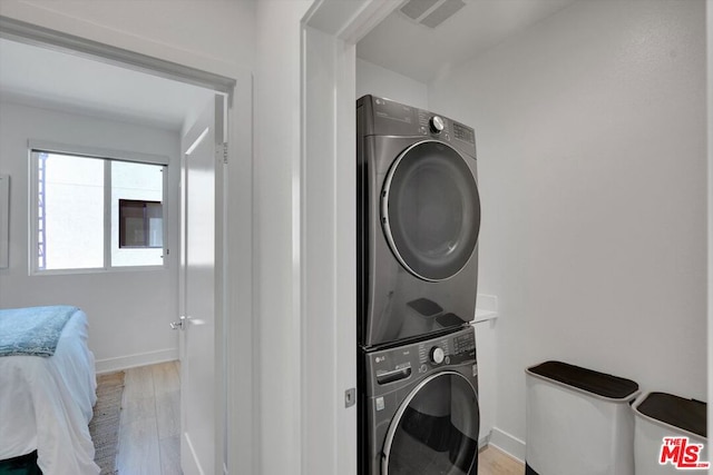 laundry room with light hardwood / wood-style floors and stacked washer / dryer