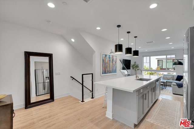 kitchen with gray cabinets, stainless steel appliances, an island with sink, light wood-type flooring, and decorative light fixtures