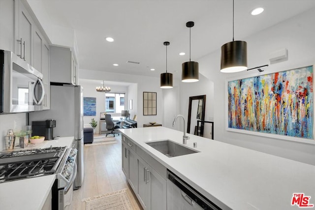 kitchen featuring stainless steel appliances, sink, gray cabinets, pendant lighting, and a notable chandelier