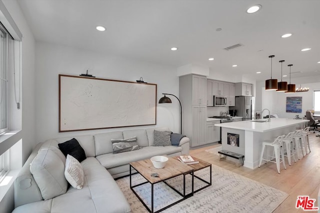 living room with sink, an inviting chandelier, and light hardwood / wood-style floors