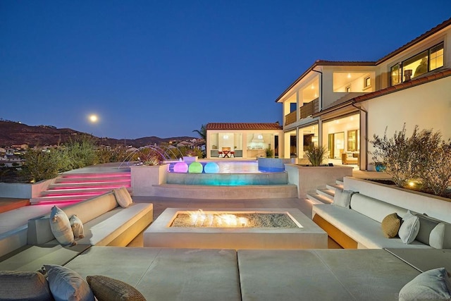 pool at night with an outdoor living space with a fire pit, a mountain view, and a patio area