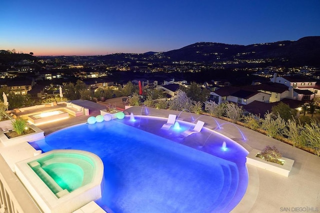 pool at dusk featuring pool water feature and an in ground hot tub