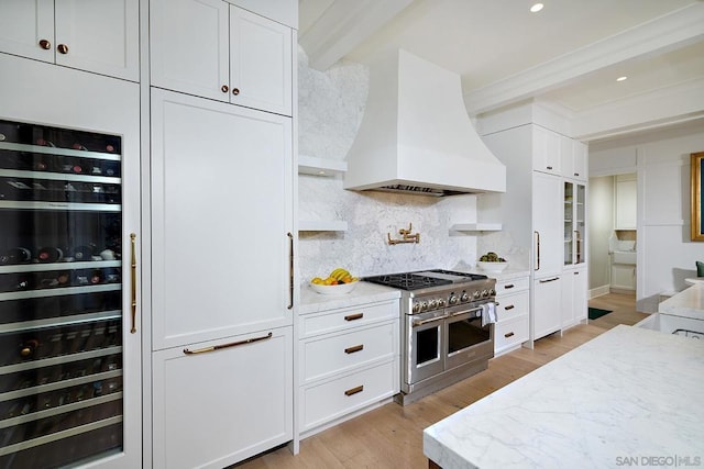 kitchen featuring custom exhaust hood, double oven range, white cabinetry, and backsplash