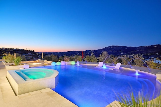 pool at dusk with pool water feature, an in ground hot tub, and a mountain view