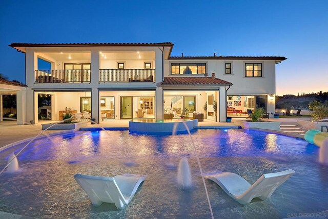 back house at dusk featuring a balcony, pool water feature, and a patio area