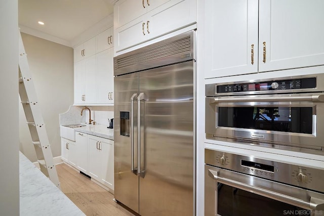 kitchen with sink, stainless steel appliances, white cabinetry, and light stone countertops