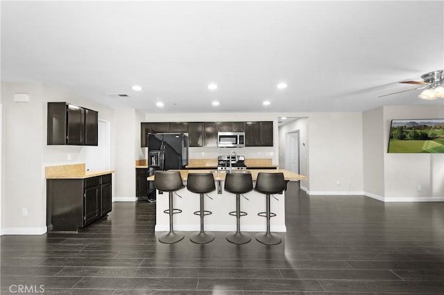 kitchen with stainless steel appliances, an island with sink, a breakfast bar area, and ceiling fan