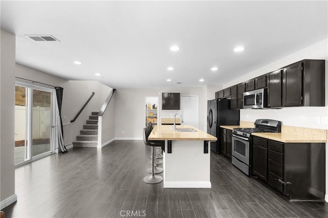 kitchen featuring sink, a breakfast bar area, stainless steel appliances, light stone counters, and a center island with sink