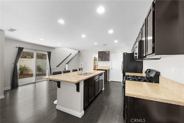 kitchen with sink, a breakfast bar area, an island with sink, stainless steel appliances, and light stone countertops