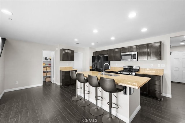 kitchen featuring sink, a breakfast bar, appliances with stainless steel finishes, a kitchen island with sink, and light stone countertops