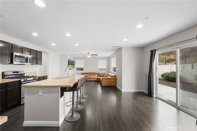 kitchen featuring appliances with stainless steel finishes, dark hardwood / wood-style floors, an island with sink, sink, and a kitchen breakfast bar