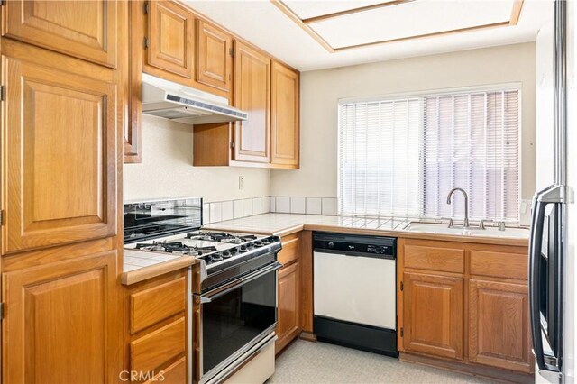 kitchen with stainless steel refrigerator, range with gas cooktop, white dishwasher, tile countertops, and sink