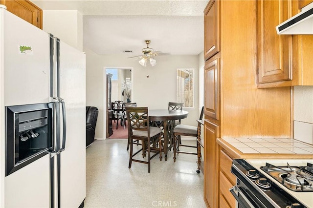 kitchen featuring range, white fridge with ice dispenser, ceiling fan, and tile counters