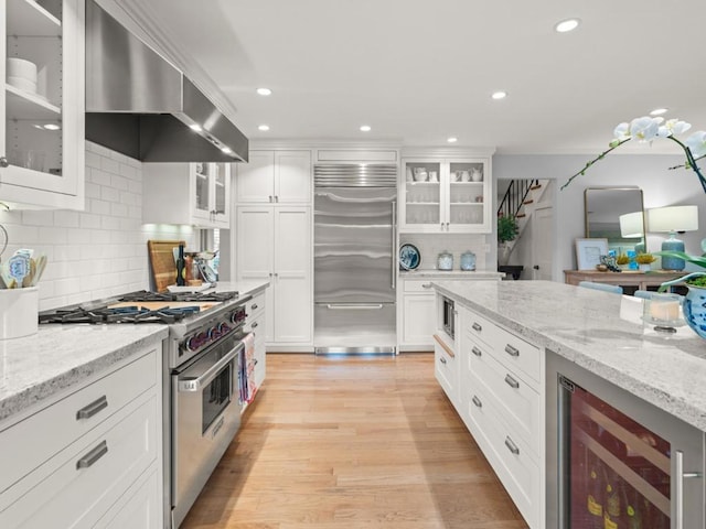 kitchen with exhaust hood, light stone countertops, premium appliances, white cabinets, and beverage cooler