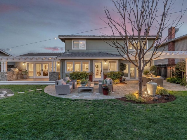 back house at dusk featuring exterior kitchen, a patio area, outdoor lounge area, and a lawn