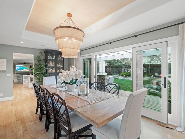 dining space with ceiling fan with notable chandelier, a tray ceiling, and light hardwood / wood-style flooring