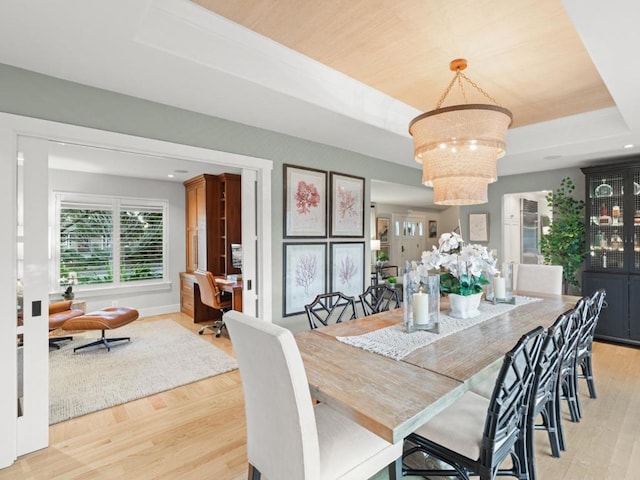 dining space with light hardwood / wood-style floors, a tray ceiling, and an inviting chandelier