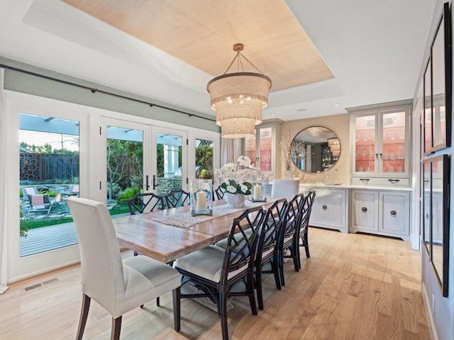 dining area with light wood-type flooring, french doors, a tray ceiling, and a chandelier