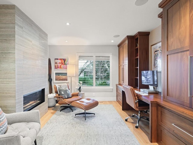 home office with built in desk, light hardwood / wood-style floors, and a tiled fireplace