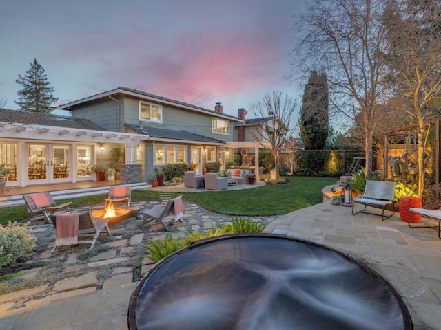 back house at dusk featuring an outdoor living space with a fire pit, french doors, a lawn, and a patio