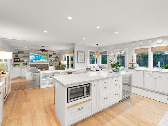 kitchen featuring a kitchen island, pendant lighting, a stone fireplace, white cabinets, and light stone counters