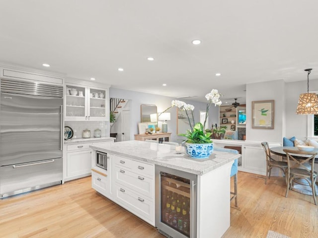 kitchen featuring a breakfast bar area, decorative light fixtures, wine cooler, built in appliances, and white cabinets