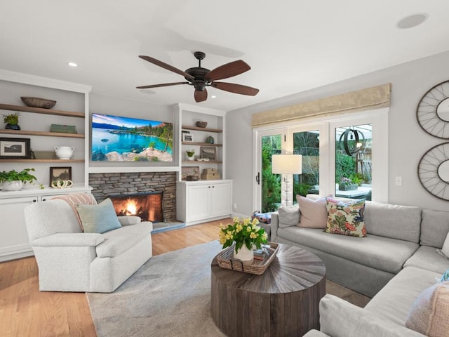 living room with ceiling fan, light hardwood / wood-style flooring, and a stone fireplace