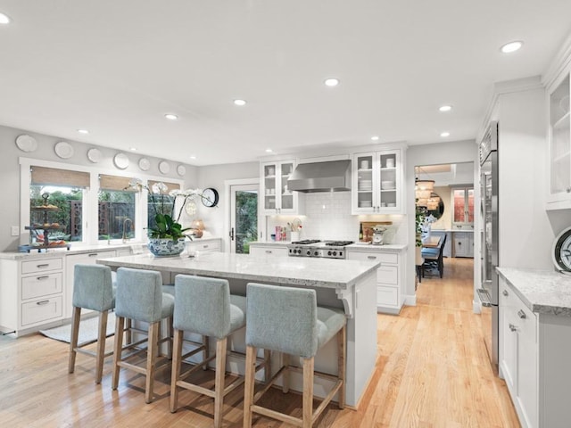 kitchen with white cabinetry, a kitchen bar, a large island, light stone countertops, and wall chimney exhaust hood