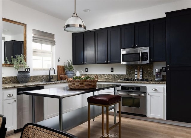 kitchen with pendant lighting, decorative backsplash, sink, light wood-type flooring, and stainless steel appliances