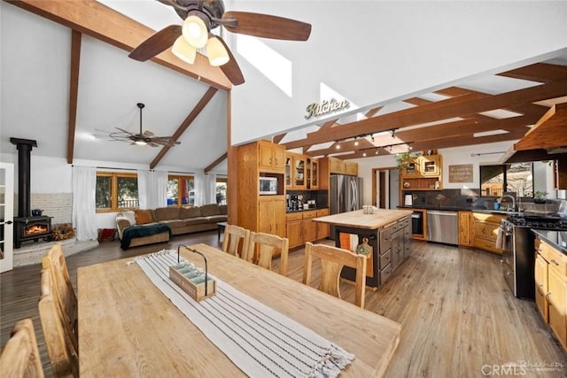 dining room featuring ceiling fan, light hardwood / wood-style floors, sink, beamed ceiling, and a wood stove