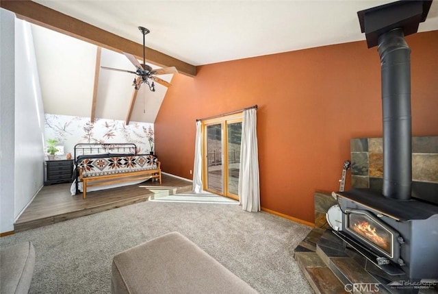 bedroom featuring ceiling fan, a wood stove, carpet floors, access to exterior, and lofted ceiling with beams