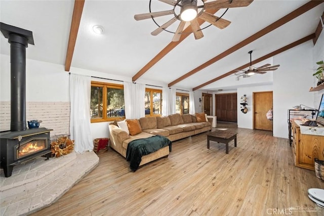 living room with light wood-type flooring, ceiling fan, a wood stove, and vaulted ceiling with beams