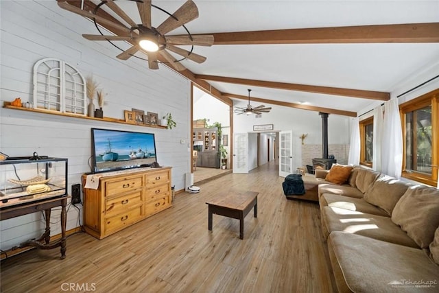 living room featuring vaulted ceiling with beams, wooden walls, a wood stove, and light hardwood / wood-style flooring