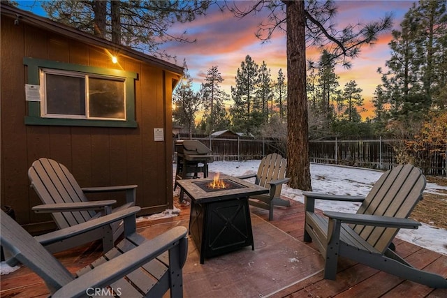 snow covered patio with an outdoor fire pit, a deck, and area for grilling