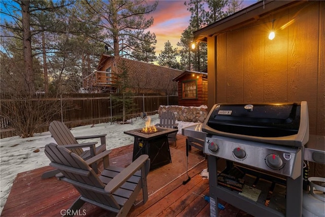 patio terrace at dusk featuring a grill, an outdoor fire pit, and a wooden deck