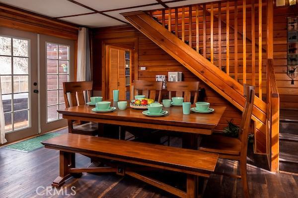 dining room with dark wood-type flooring, french doors, wooden walls, and plenty of natural light