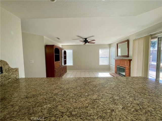 unfurnished living room with a brick fireplace, light tile patterned floors, and ceiling fan